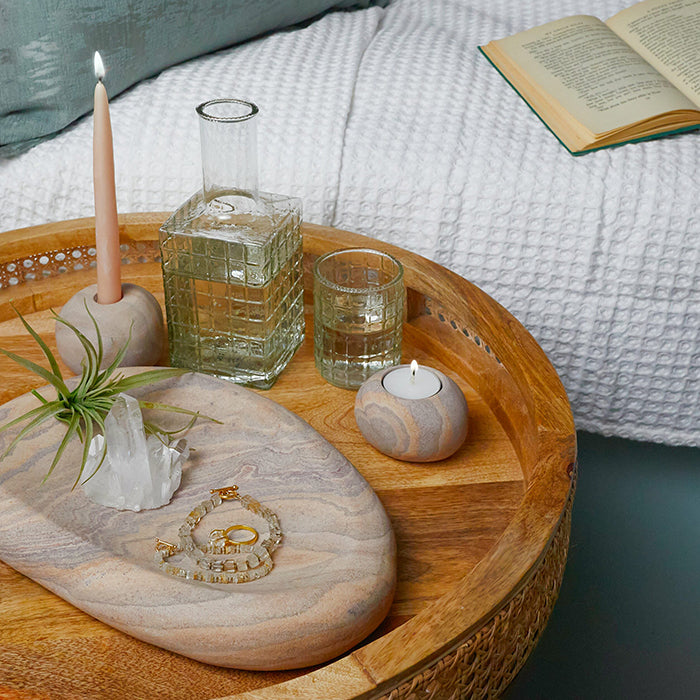 Elegant nightstand styling with natural sandstone accents, including a taper candle holder and jewelry display, for a modern home aesthetic.