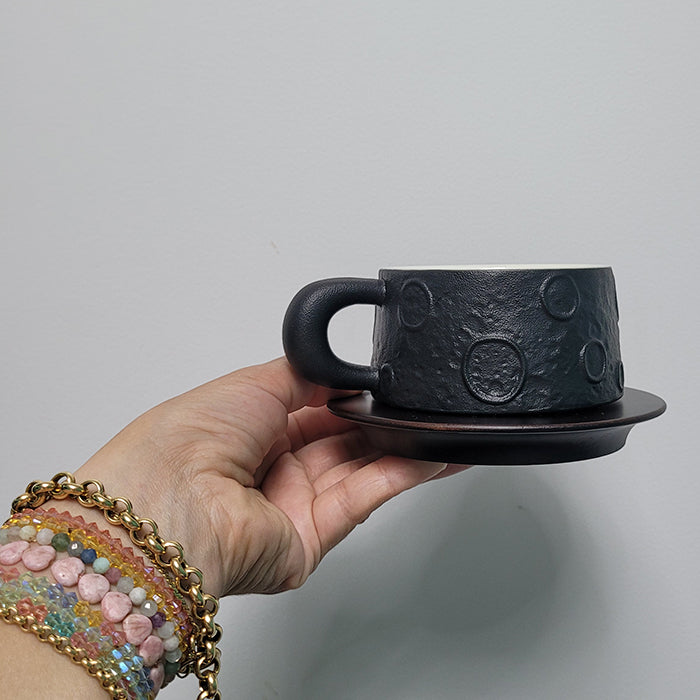 Hand holding minimalist black ceramic coffee mug with wood saucer