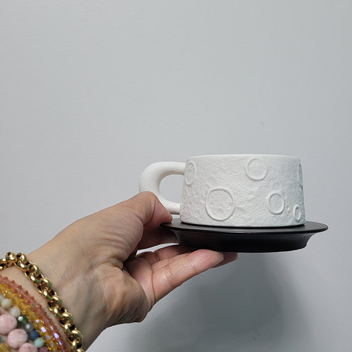 Hand holding white matte ceramic mug with wood saucer